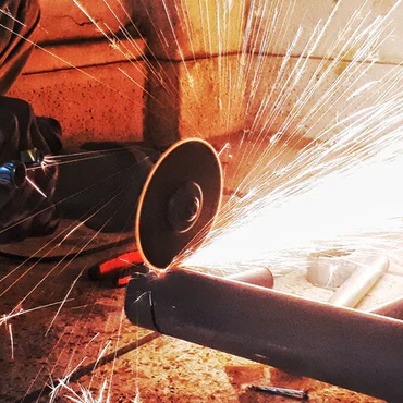 Worker grinding a metal pipe with a handheld grinder; bright sparks fly in a workshop