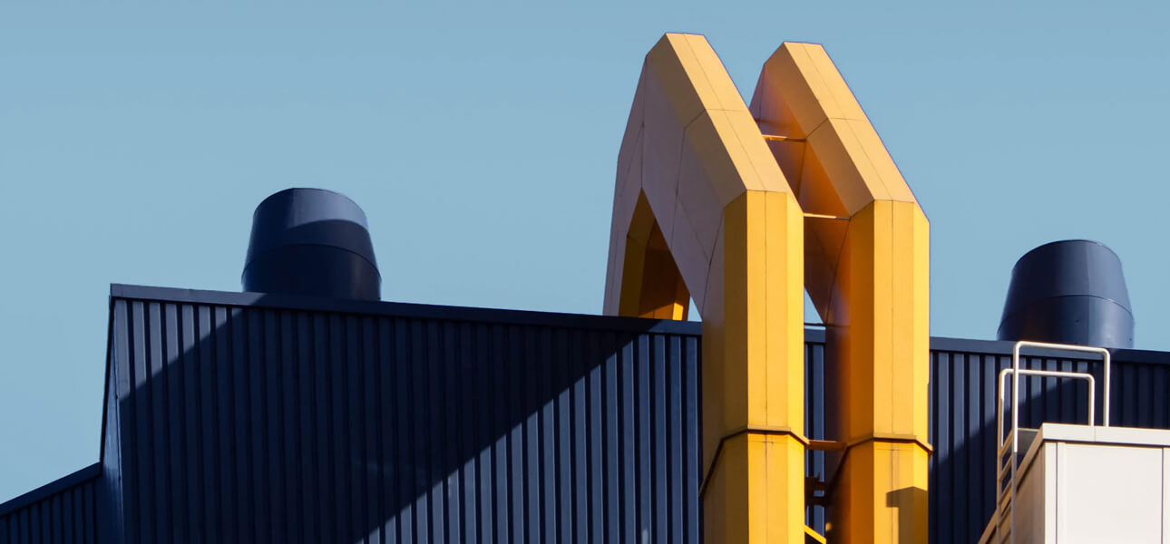 Two yellow arch like structures rising from a dark blue building roof against a clear blue sky